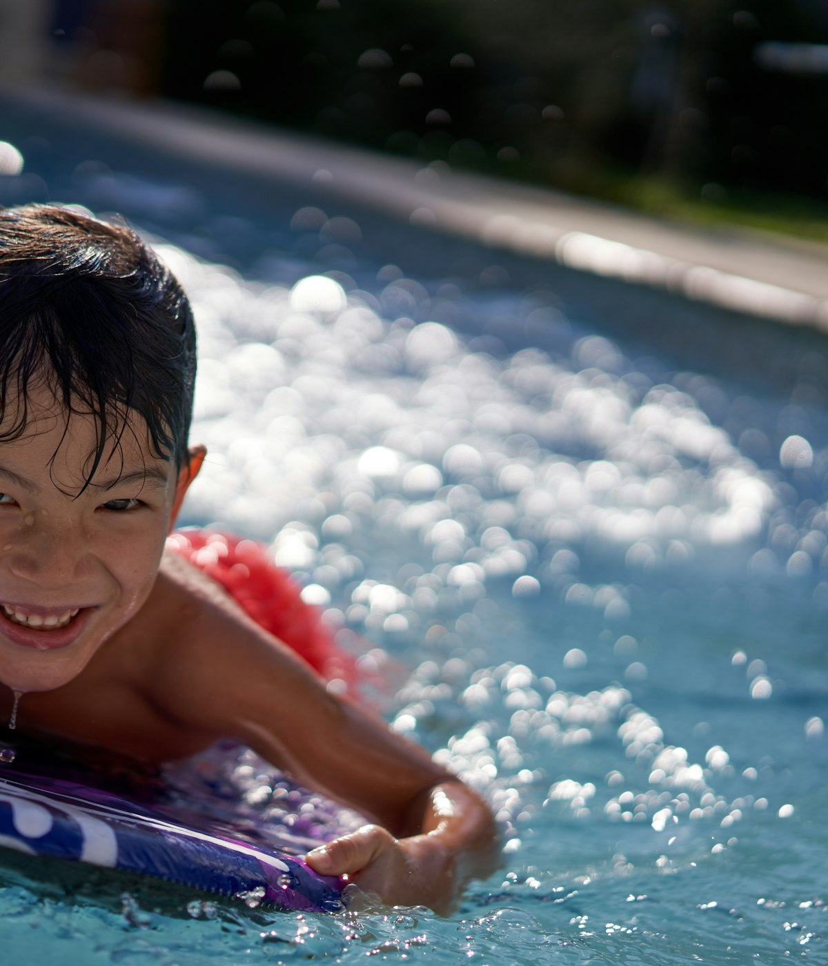 A smiling boy in a pool, holding on to a kickboard