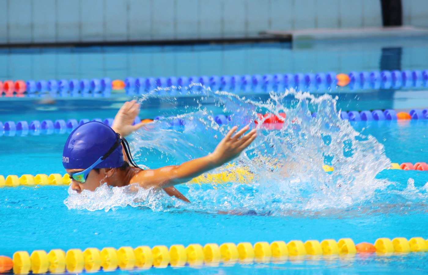 A swimmer in a cap and goggles swimming freestyle down a lane